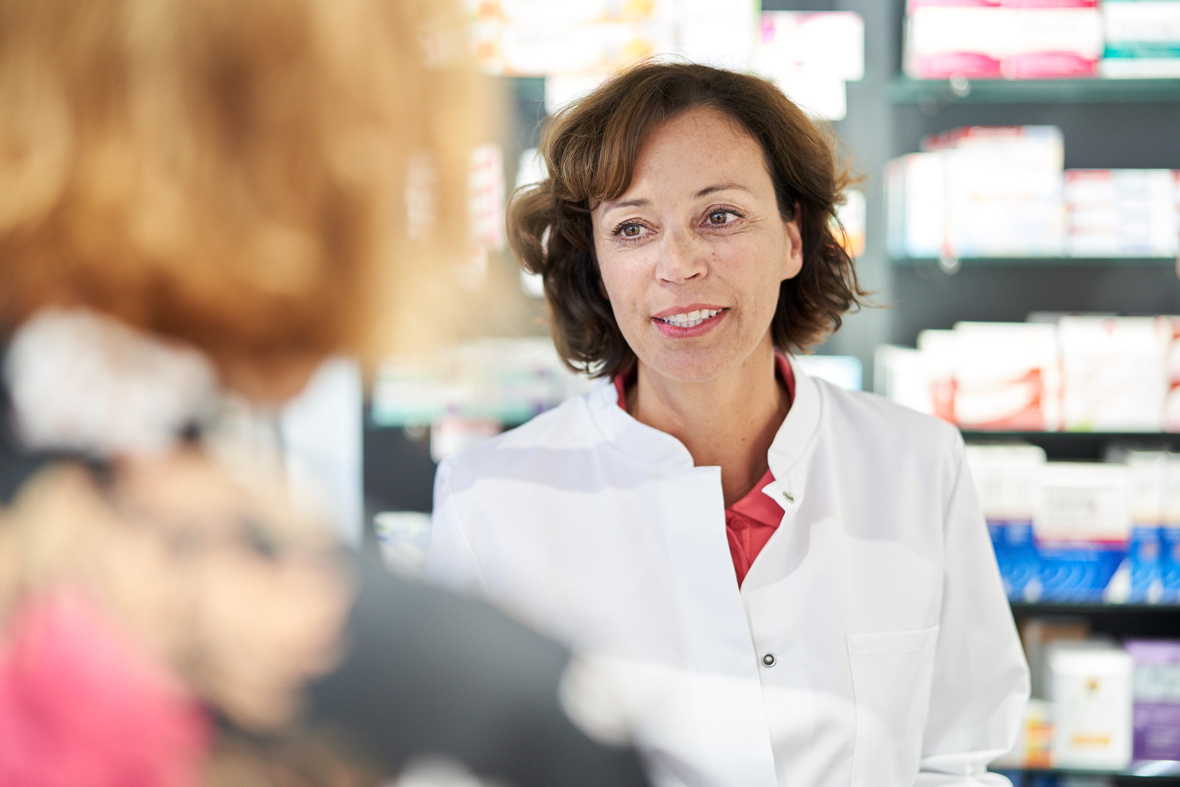 A pharmacist in a white coat serves a customer.